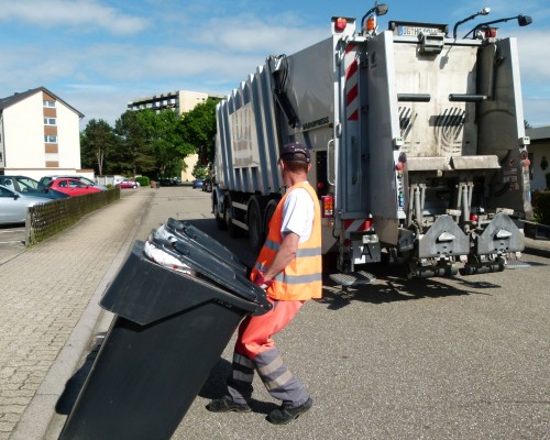 Das Foto zeigt einen Müllwerker beim Leeren von grauen Tonnen. Im Hintergrund ist die Rückseite eines Müllautos sichtbar. (Foto: Martin Schmidt/Abfallwirtschaftsbetrieb)