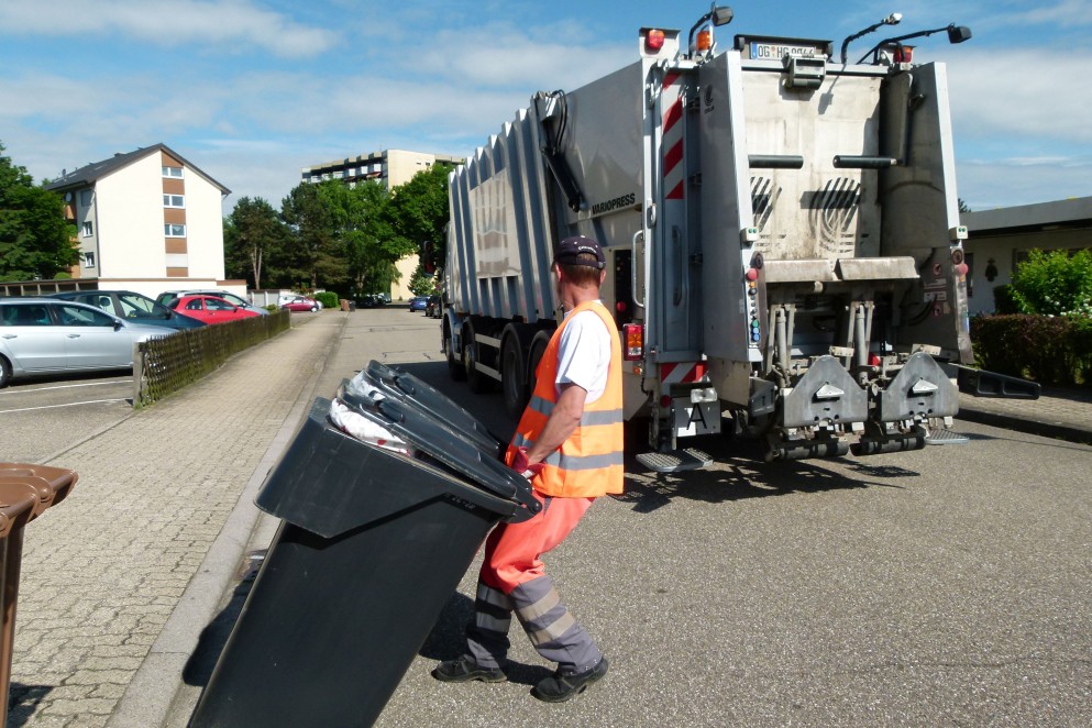 Das Foto zeigt einen Müllwerker beim Leeren von grauen Tonnen. Im Hintergrund ist die Rückseite eines Müllautos sichtbar. (Foto: Martin Schmidt/Abfallwirtschaftsbetrieb)