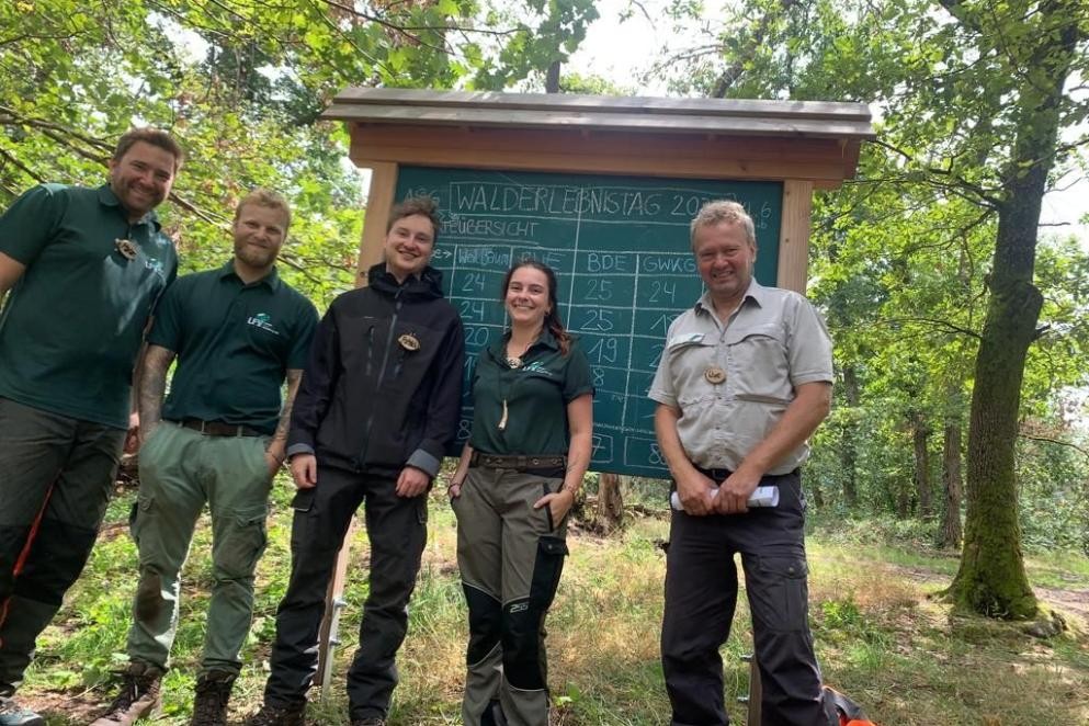Fünf Mitarbeitende des Forstamts stehen in Arbeitskleidung im Wald.