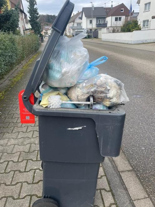 Das Foto zeigt eine überfüllte graue Mülltonne am Straßenrand. Die Tonne kann nicht geschlossen werden, weil sich Müllsäcke darauf stapeln. Foto MERB, Achern