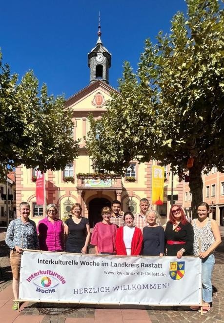 Vielfalt sichtbar machen: In wenigen Tagen startet im Landkreis Rastatt die Interkulturelle Woche mit vielen Mitmach-Aktionen. Die Organisatoren freuen sich auf eine rege Beteiligung. Foto: Miriam Fischer/Stadt Rastatt. Die Organisatorinnen und Organisatoren stehen vor dem historischen rathaus der Stadt Rastatt und halten den Banner der Interkulturellen Woche in die Kamera.. Foto: Miriam Fischer/Stadt Rastatt.