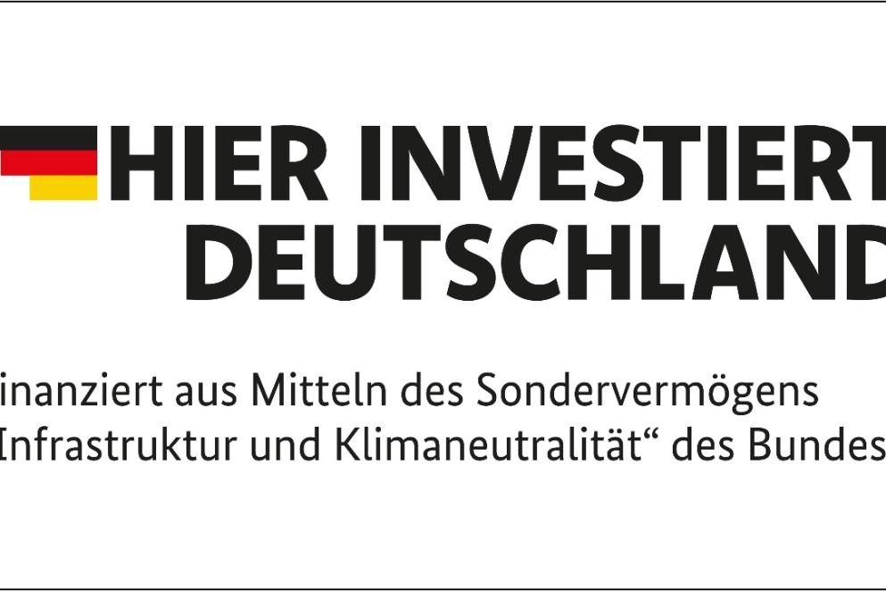 Die offizielle Programmmarke „Hier investiert Deutschland“ kennzeichnet Projekte, die aus dem Sondervermögen für Infrastruktur und Klimaneutralität des Bundes finanziert werden. Credit: Bundesregierung Das Foto zeigt die offizielle Programmmarke „Hier investiert Deutschland“ kennzeichnet Projekte, die aus dem Sondervermögen für Infrastruktur und Klimaneutralität des Bundes finanziert werden. Credit: Bundesregierung