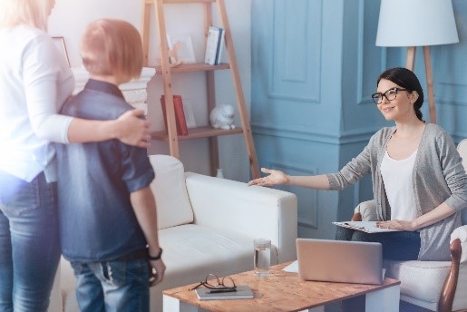 Das Foto zeigt drei Personen, zwei Personen stehen und eine Person sitzt. 