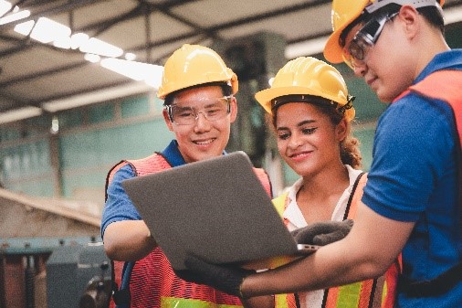 Das Foto zeigt drei Personen, die um einen Laptop stehen.